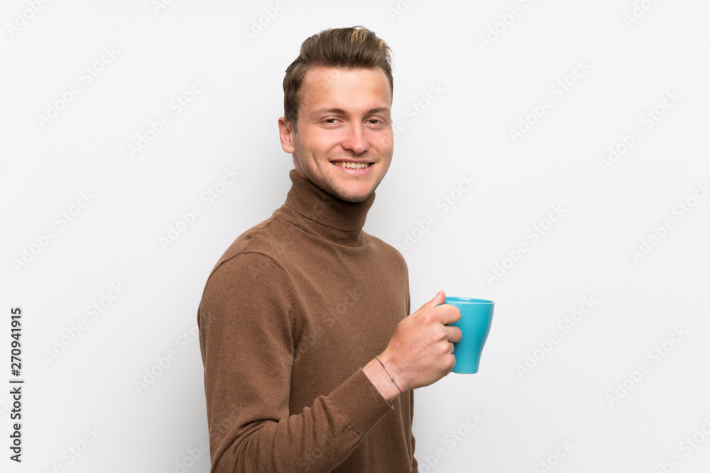 Blonde man over isolated white wall holding a hot cup of coffee Blonde man over isolated white wall holding a hot cup of coffee