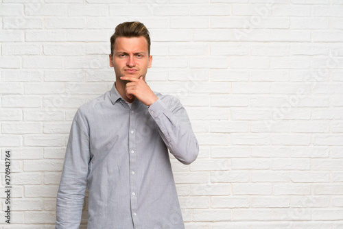 Blonde man over white brick wall thinking