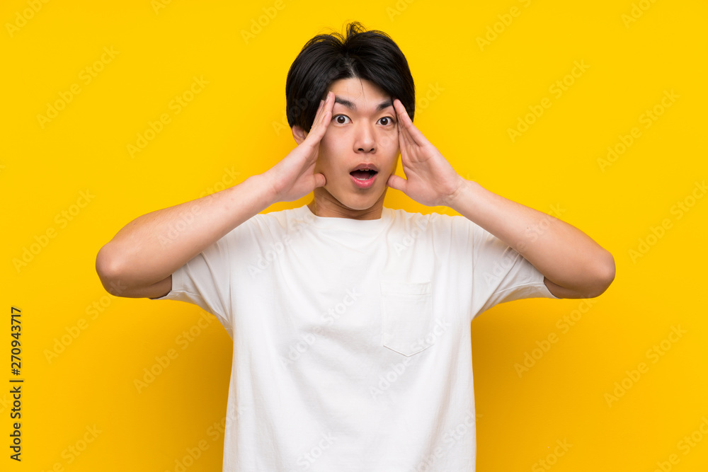 Asian man over isolated yellow wall with surprise expression Asian man over isolated yellow wall with surprise expression