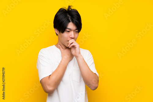 Asian man over isolated yellow wall is suffering with cough and feeling bad