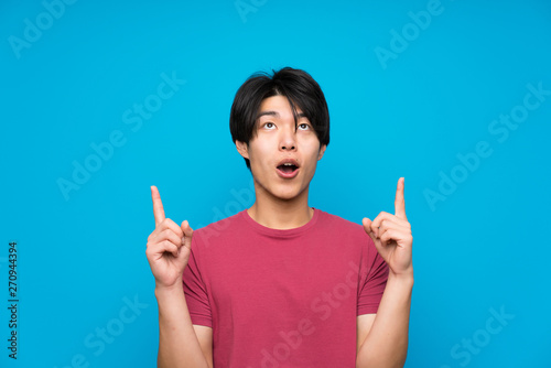 Asian man with red shirt over isolated blue wall pointing with the index finger a great idea