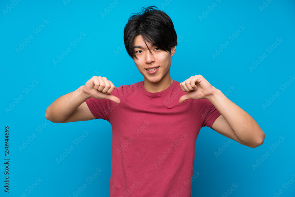 Fototapeta premium Asian man with red shirt over isolated blue wall proud and self-satisfied