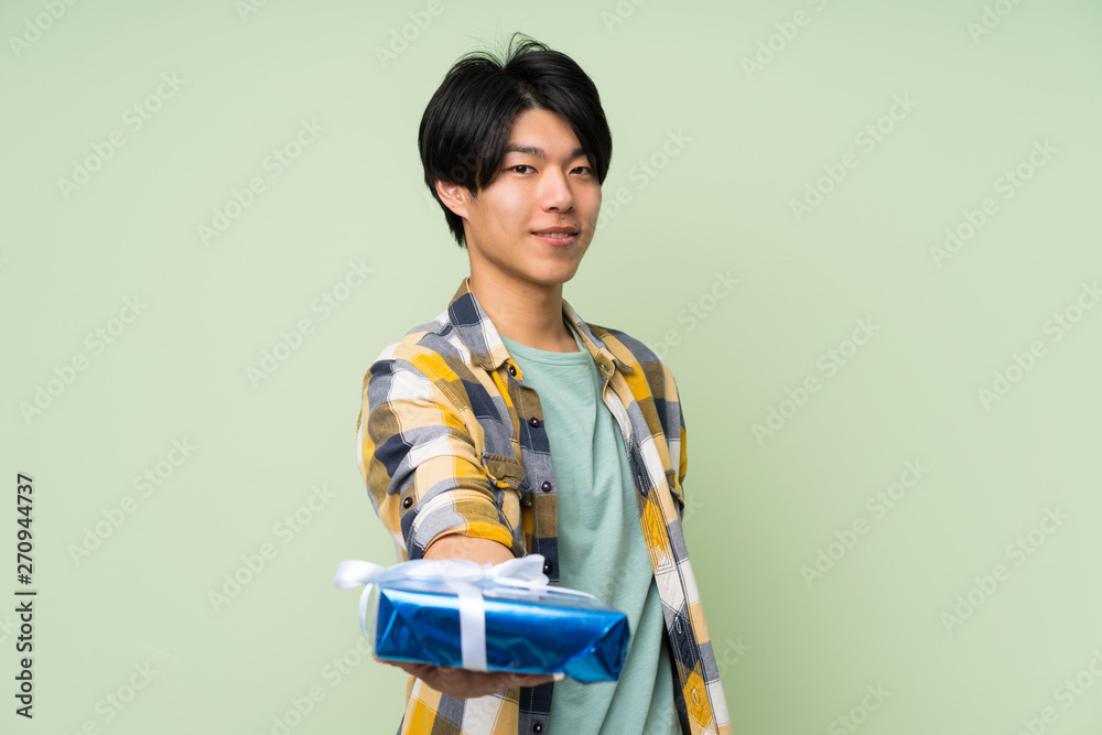 Asian man over isolated green wall holding gift box Asian man over isolated green wall holding gift box