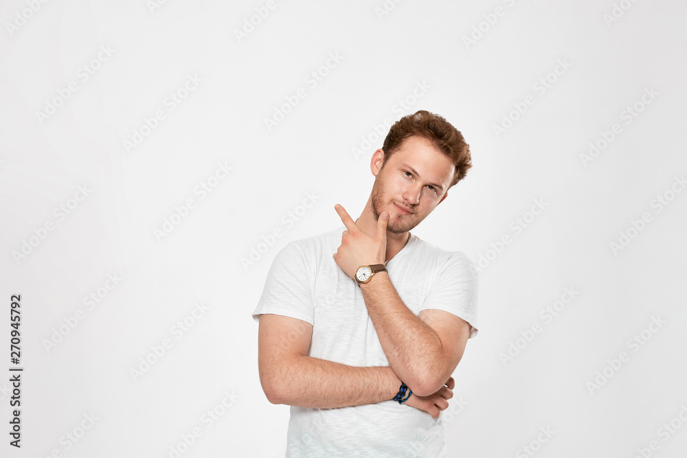 Young bearded confident man with hand raised on chin and looking at the camera.