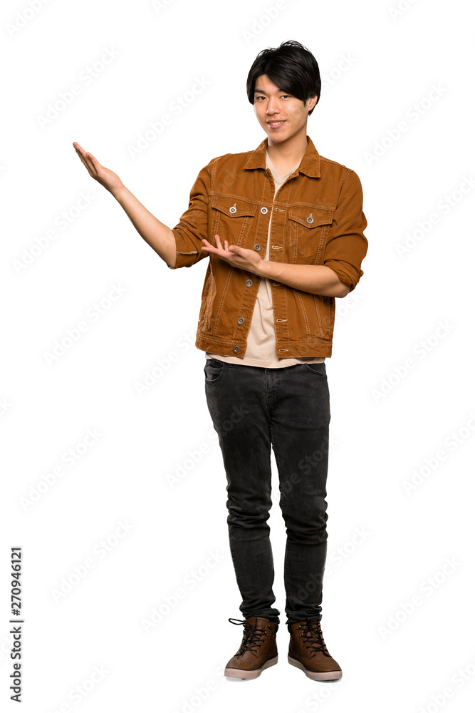 A full-length shot of a Asian man with brown jacket extending hands to the side for inviting to come over isolated white background A full-length shot of a Asian man with brown jacket extending hands to the side for inviting to come over isolated white background