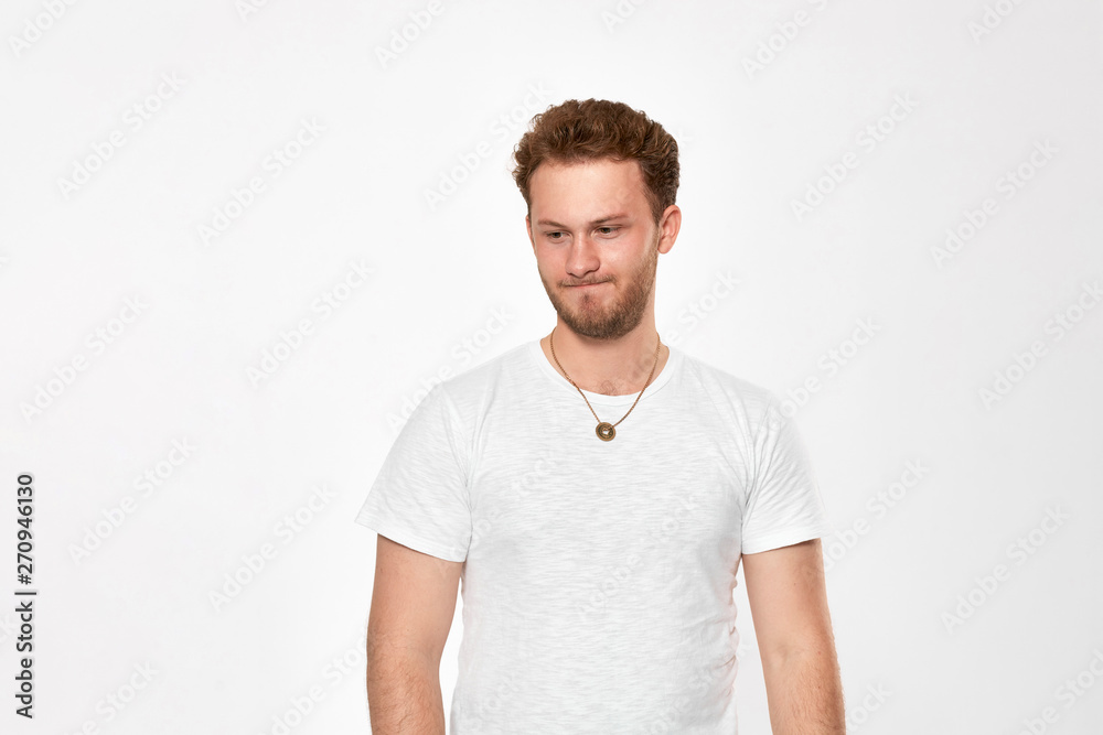 Upset handsome young man looks down and keeps arms crossed Upset handsome young man looks down and keeps arms crossed