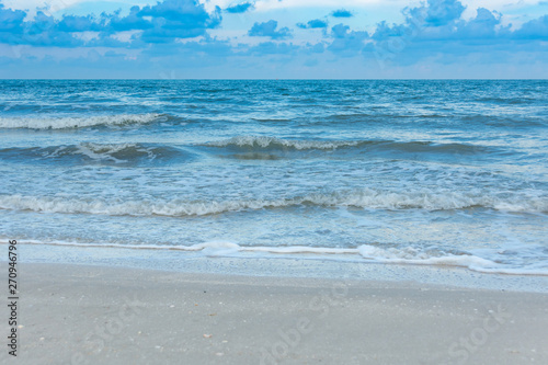 The blue sea creates waves by the white sea breeze blowing into the shore.