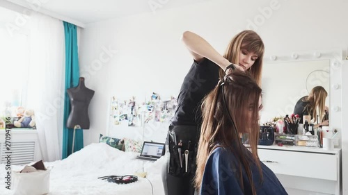 Timelapse shot of cute young female barber enjoying working with a beautiful young brunette model, doing fresh trendy hairstyle on her long curly hair using curling iron, hairbrush, hair spray