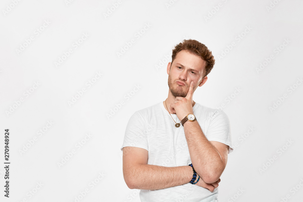 Upset handsome young man looks at the camera and keeps one hand on a face. Upset handsome young man looks at the camera and keeps one hand on a face.