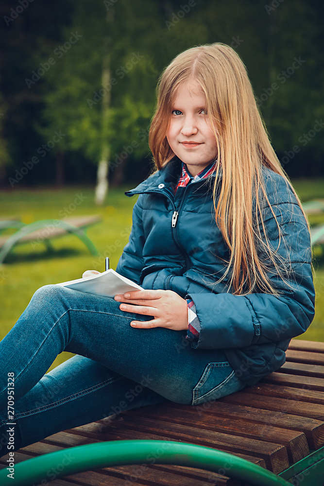 Girl with blond hair writing a letter on a wooden chaise longue in the spring Girl with blond hair writing a letter on a wooden chaise longue in the spring