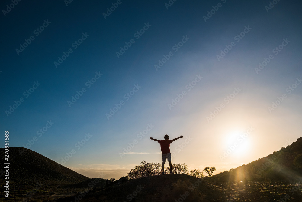 teenager in mountain stay with open arms alone and with headphones and a great sunset - jogging  and fit - sun at the background and sky - freedom concept - caucasian 20s