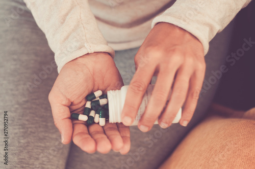 Subject medicine health and pharmaceuticals. Close-up macro young caucasian woman hands pulling out a green blister. Packing two white round pills in home clothes at home on the bed.