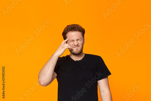 Studio shot of a bearded young man pointing a finger at the temple. Concept of a positive thinking.