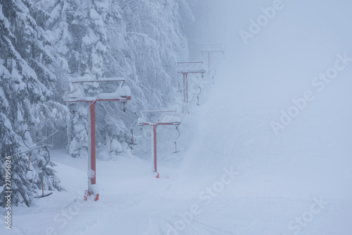 Frozen ski lift covered with snow. Hard winter conditions, snowfall and fog.