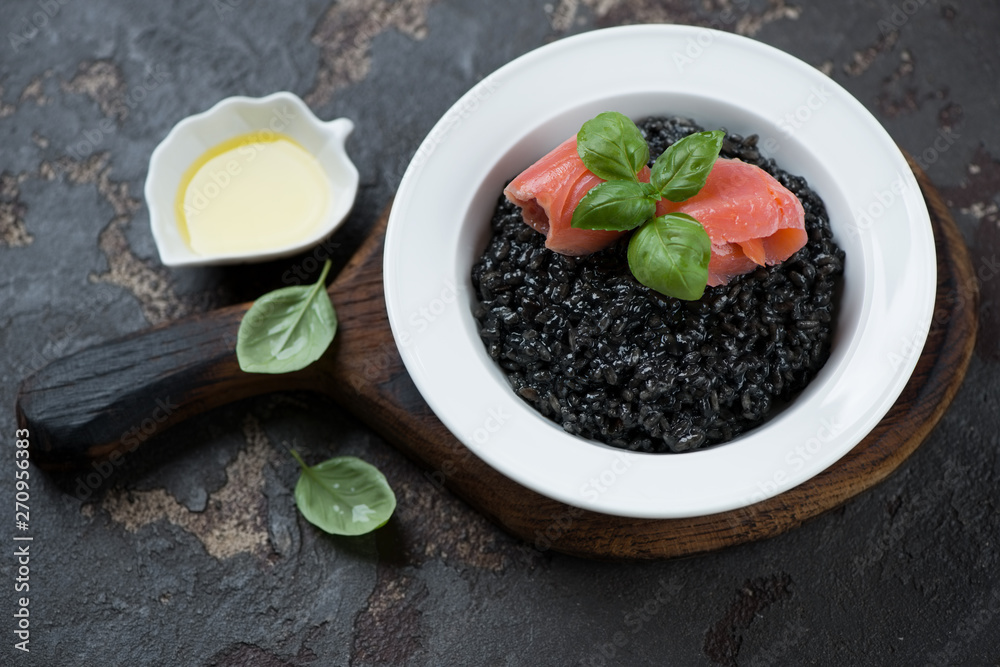 Plate of risotto with squid-ink and salmon fillet, studio shot on a brown stone background Plate of risotto with squid-ink and salmon fillet, studio shot on a brown stone background