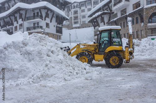 Yellow excavator, tractor with snowplow removing snow after heavy snowfall.. Winter time maintenance in snowfall.