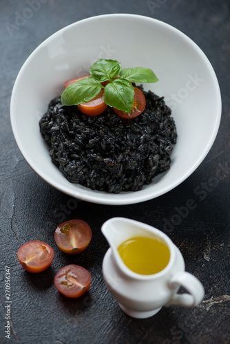 Risotto with squid-ink, cherry tomatoes, fresh green basil and olive oil, vertical shot on a dark brown stone background