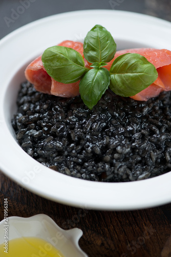 Close-up of squid-ink risotto served with salmon fillet and green basil in a white plate