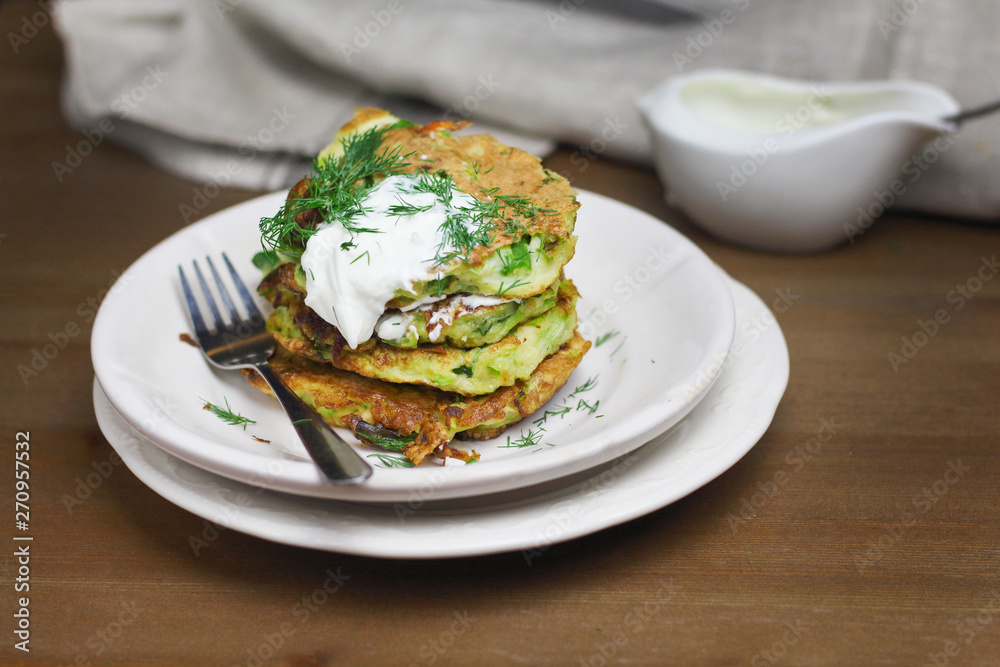 Proper nutrition, vegetarian breakfast gluten free,zucchini courgette pancakes with beans, mint on white plates with sour greek yogurt, black background, towel, fork, knife on wooden surface