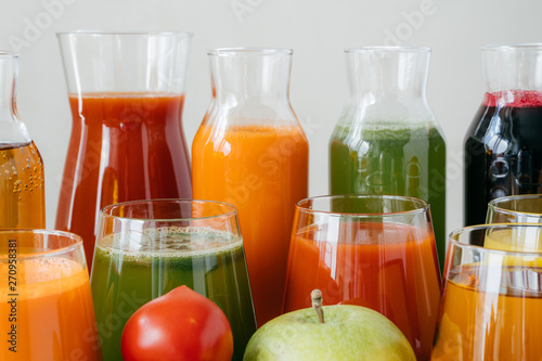 Close up shot of glass bottles filled with colorful juice made of various vegetables and fruit, red tomato and green apple in foreground. Fresh detox drink