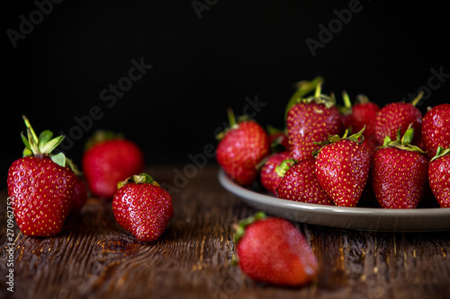 Strawberries scattered and in a plate on a wooden background.