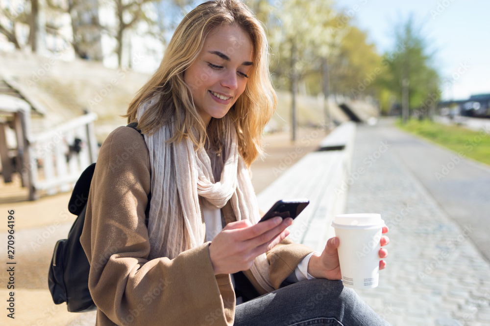 Pretty young woman using her mobile phone while holding cup of coffee in the street. Pretty young woman using her mobile phone while holding cup of coffee in the street.