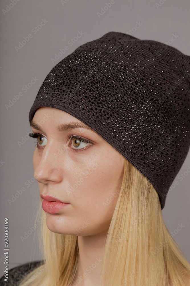 Portrait of a beautiful young girl in a stylish headdress with natural makeup on a gray background.