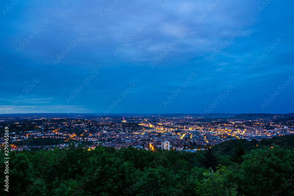 Germany, Magic lights of houses of big city stuttgart from above behind green forest in beautiful twilight mood from mount rubble