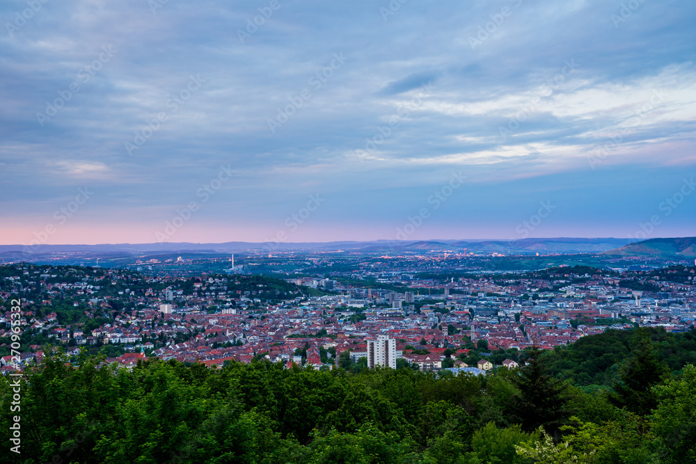 Germany, Above green treetops and red roofs of skyline of large city stuttgart from hilltop of mount rubble at sunset in summer