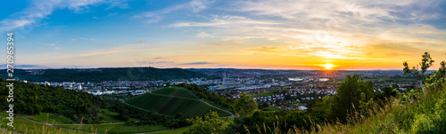 Germany, XXL panorama of romantic orange sunset sky over houses of beautiful metropolis city stuttgart in valley between vineyards from above