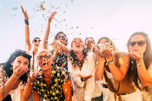 People having fun in party celebration friends concept - group of young and adult women all together laughing blowing coloured confetti - friendship and love for lifestyle with mixed active generation photo