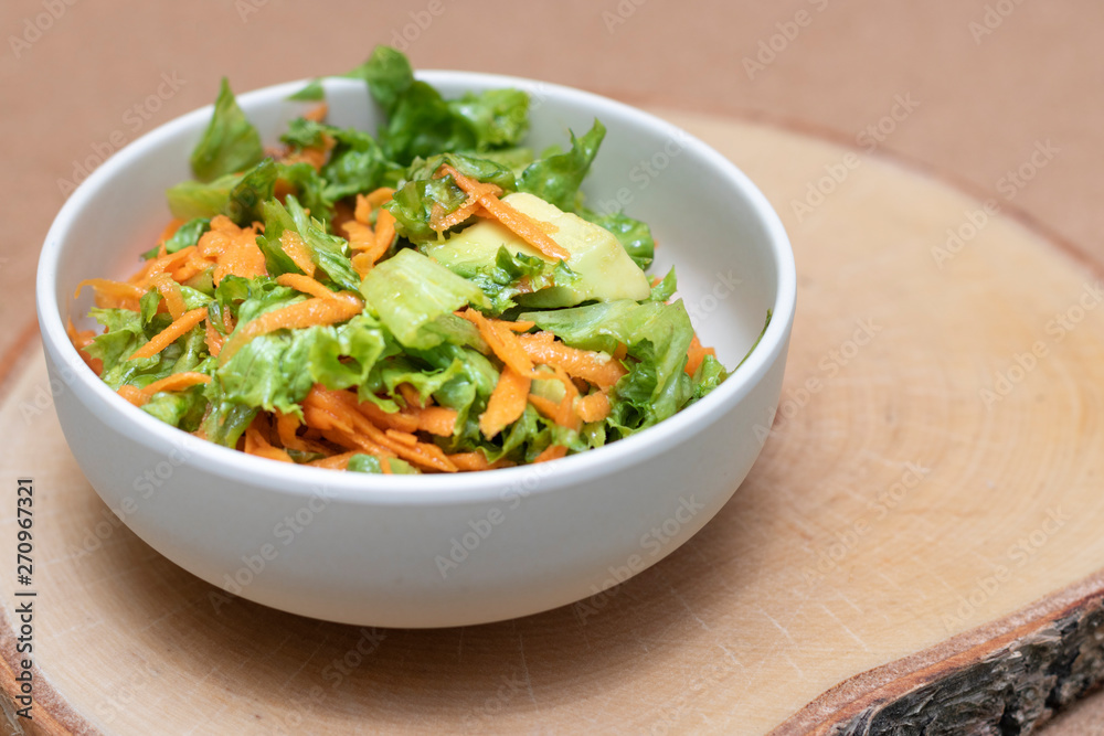 Vegetable salad with avocado, carrot, greens on wooden background