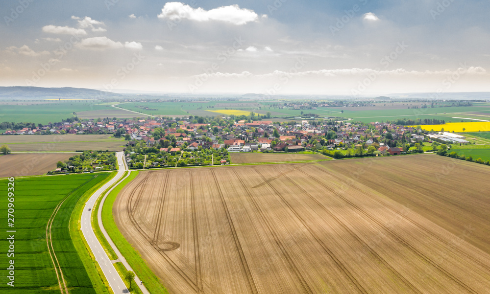 Aerial view of a road between the fields with a village and a dramatic sky with clouds in the background, aerial view