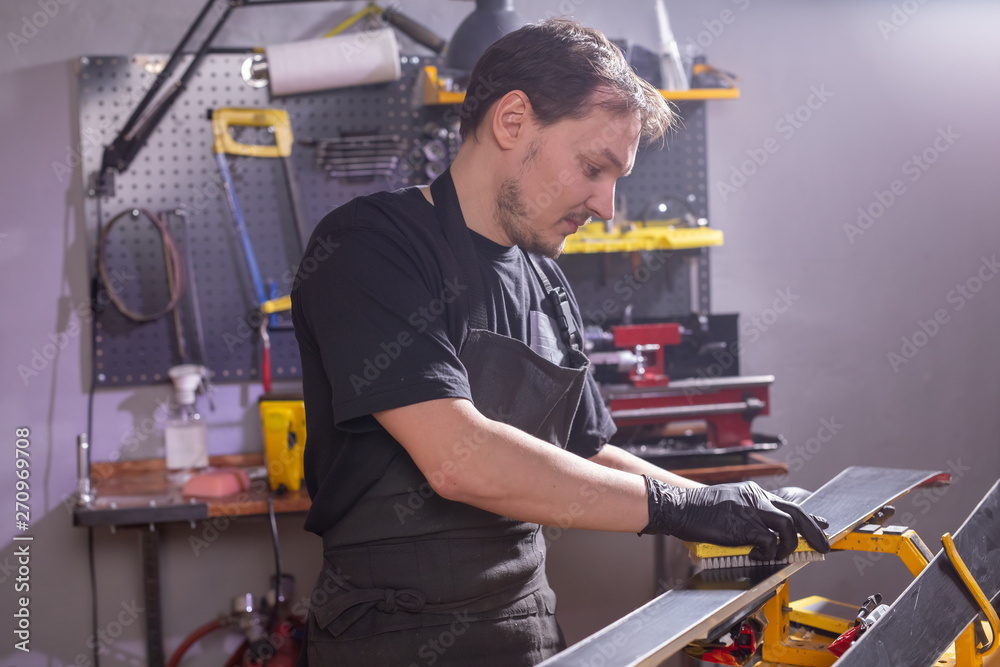 Repair, service and people concept - a man repairing the ski by rubbing a paraffin