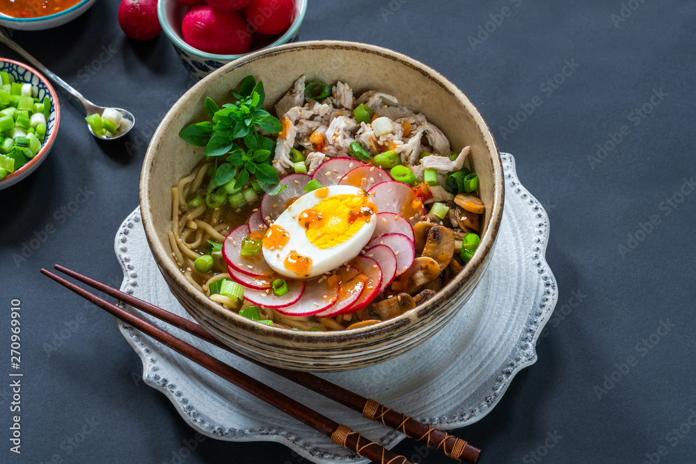 Ramen noodles with chicken, egg, mushrooms and radish sprinkeld with chili sauce and sesame seeds - high angle view