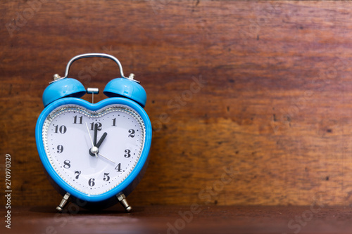 Heart shaped alarm clock on wooden background. One O Clock