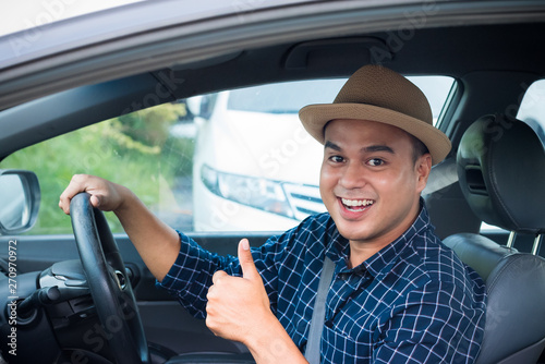 Young asian man showing thumbs up while driving car with copy space. © Nopphon