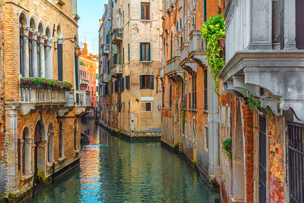 Venetian canal with gondola and colorful facades of old medieval houses in Venice, Italy