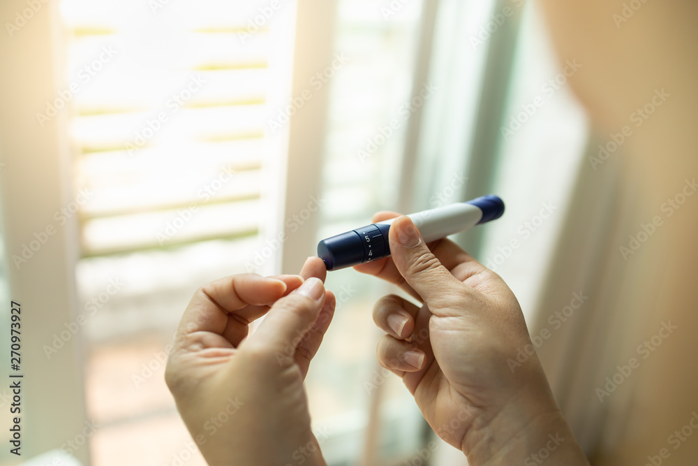 Close up of woman hands using lancet on finger to check blood sugar level by Glucose meter in the morning. Use as Medicine, diabetes, glycemia, health care and people concept. Close up of woman hands using lancet on finger to check blood sugar level by Glucose meter in the morning. Use as Medicine, diabetes, glycemia, health care and people concept.