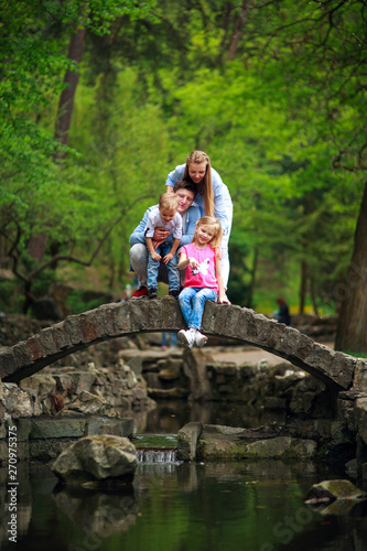 Happy young family with children in summer green park on stone bridge over the river in forest
