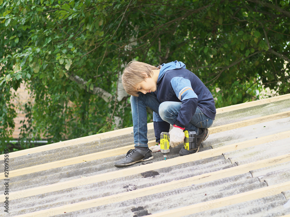 Teenager boy help to repair the roof of a home with hammer and drill