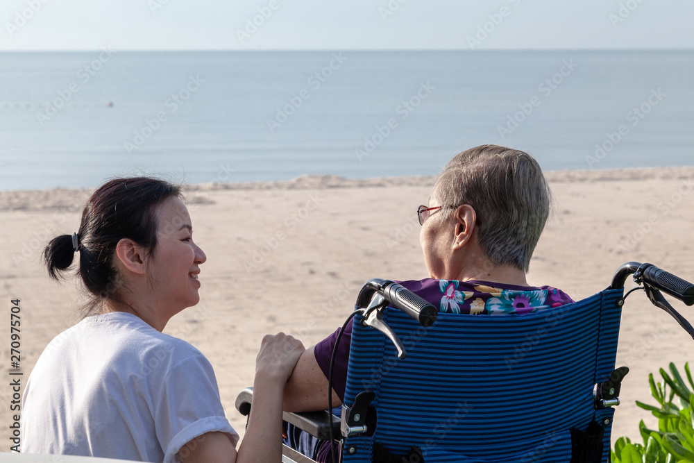 Mother and daughter sit together in front of the beach looking at each other.
