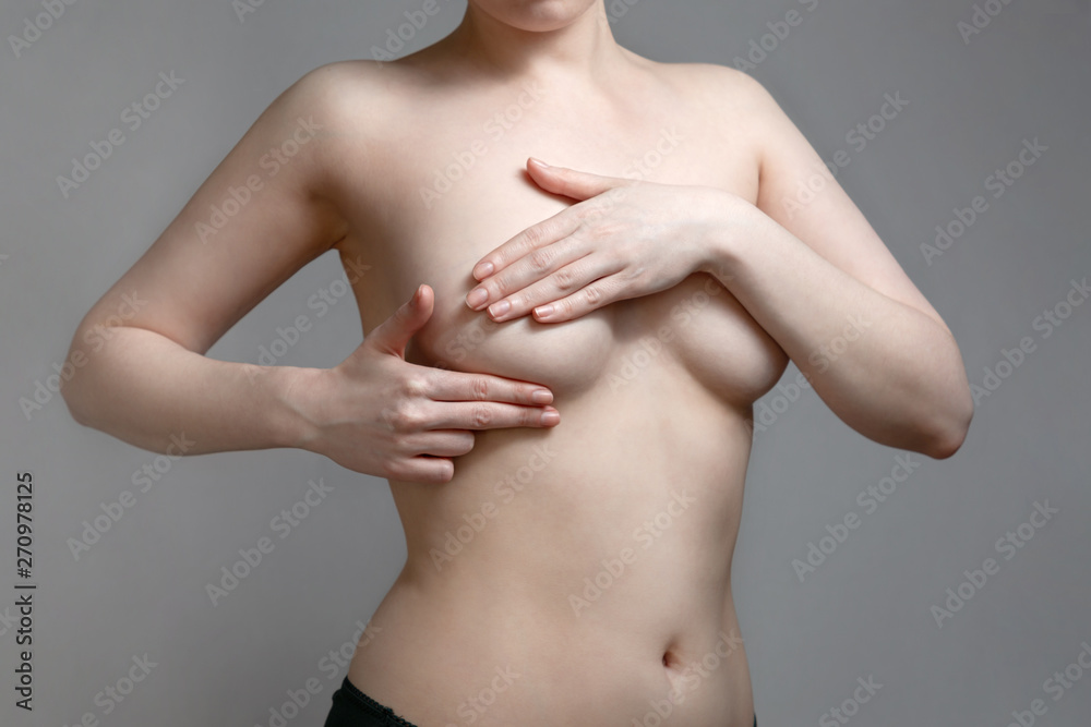 A young woman conducts an independent examination for the presence of tumors in the breast. Gray background. The concept of women's breast diseases A young woman conducts an independent examination for the presence of tumors in the breast. Gray background. The concept of women's breast diseases