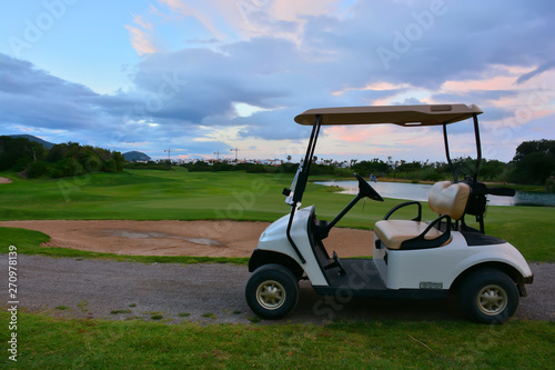 Golf cart on a golf course. Green field and cloudy blue sky. Spring landscape with grass and trees. Vibrant colors