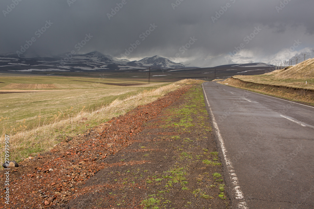 the road among the steppe on the background of snow-capped mountains under a stormy sky