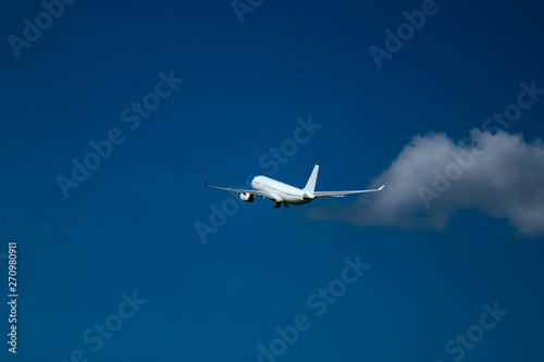 Big white airplane in the bright blue sky after takeoff with the cloud nearby