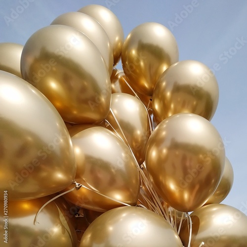 holidays, birthday party, wedding decoration concept - many metallic gold helium balloons on blue sky. Close up and abstract of vintage gold balloons for background