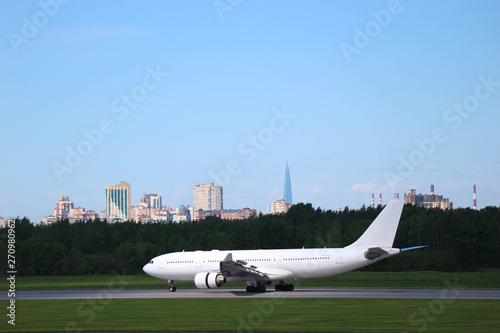widebody white airplane with two engines on the runway after landing in the airport with the silhouette of the city on the background