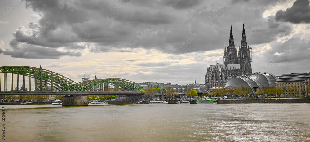 Schwarz Weiss Köln Panorama mit Kölner Dom, Musical Dome, Hohenzollernbrücke mit grünen Akzenten der Bäumen und Brücke. Bewölter Himmel mit Blick auf die Altstadt.