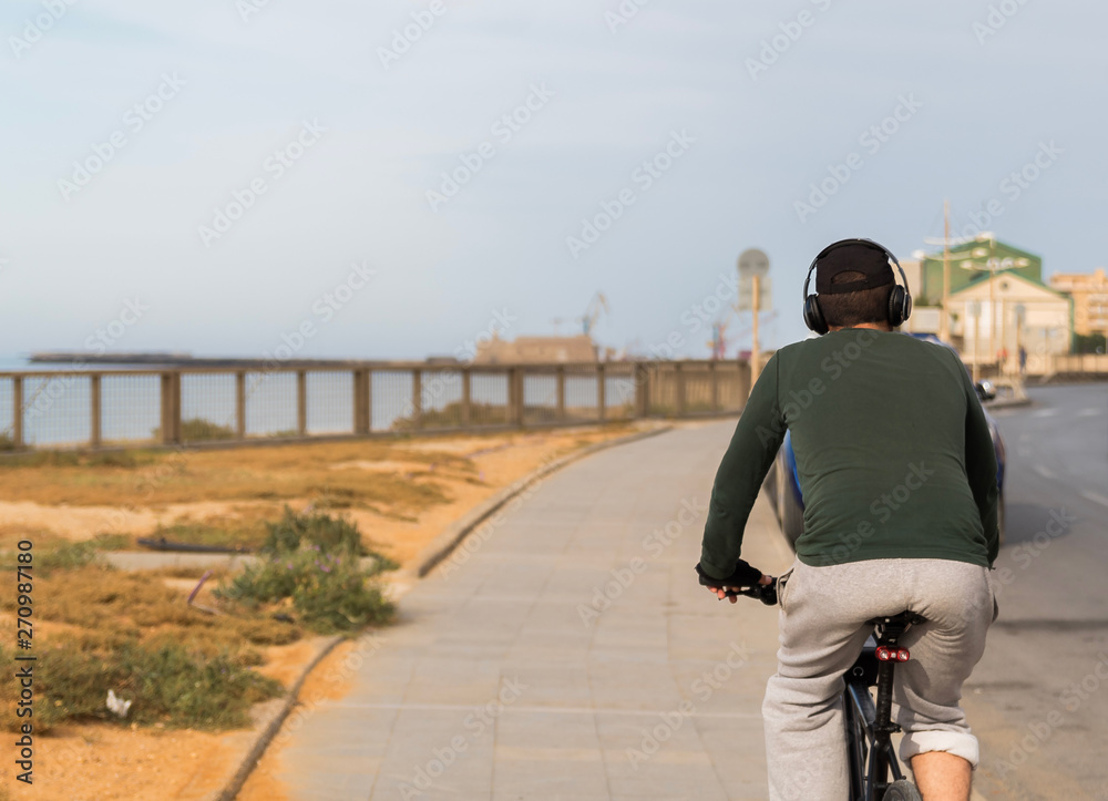 rear view of a man with headphones riding the bicycle by the sea